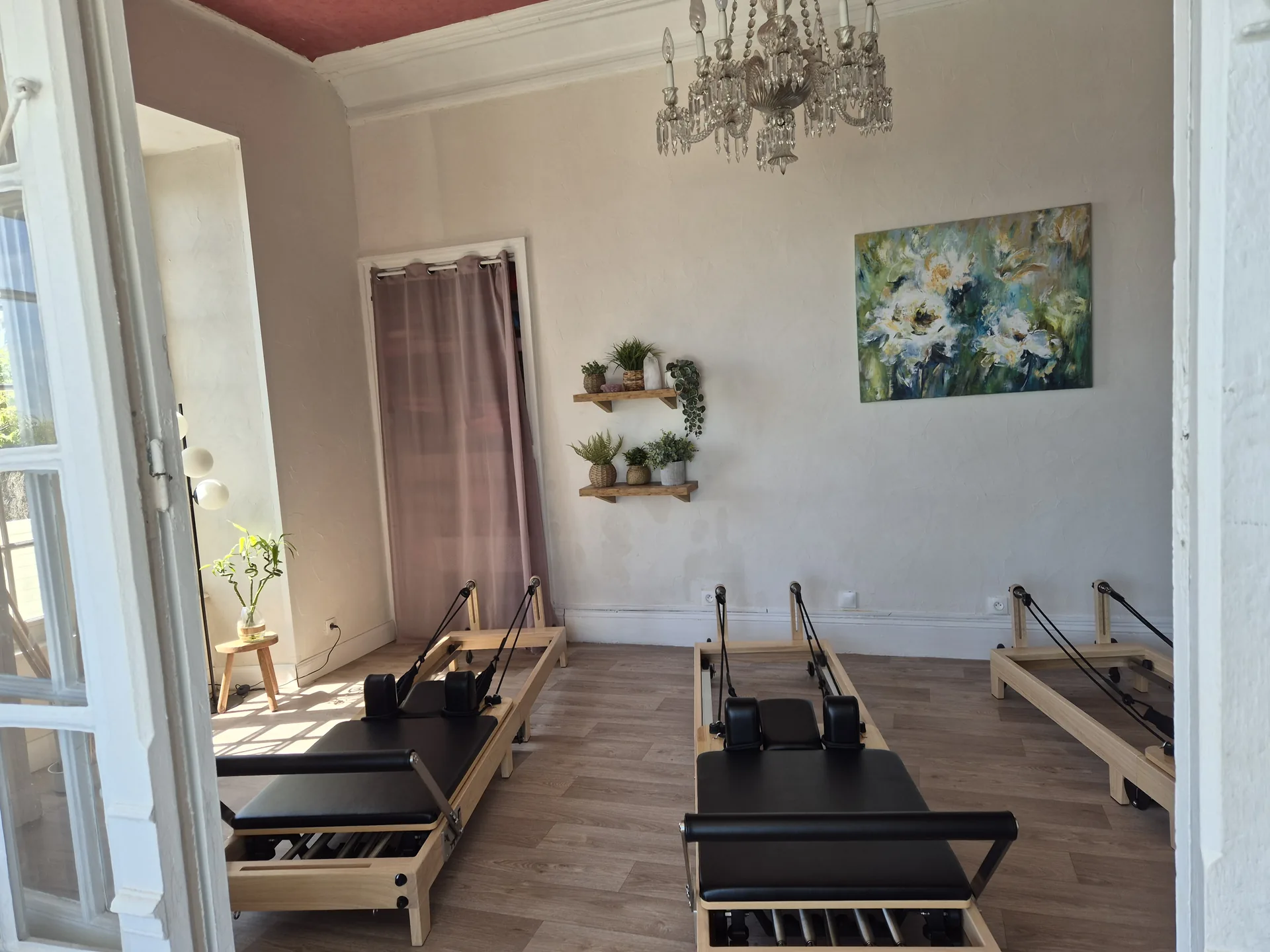 Studio de Pilates intérieur avec trois Reformers, lustre en cristal et grandes fenêtres